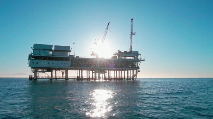 在一个晴朗的早晨，在加州长滩/洛杉矶附近，黄昏时分关闭海上石油和天然气钻井平台与远处的货船