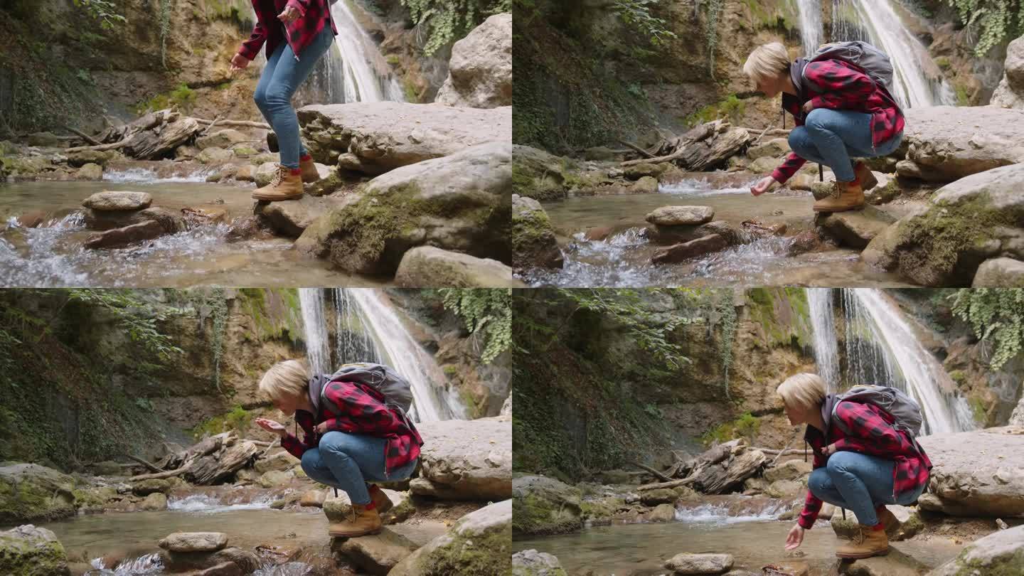 一位背包客在瀑布边用手舀水，喝着山河的清凉水。