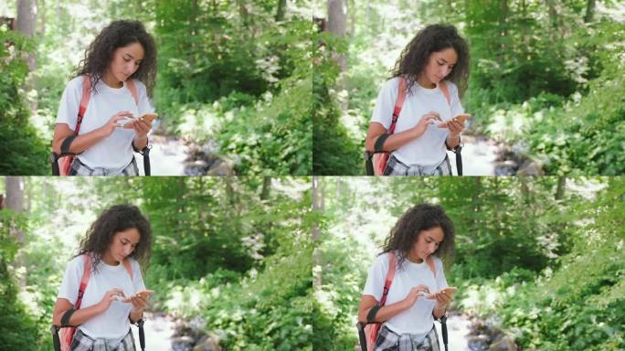 卷发女孩在森林里用智能手机在河边徒步旅行的照片。