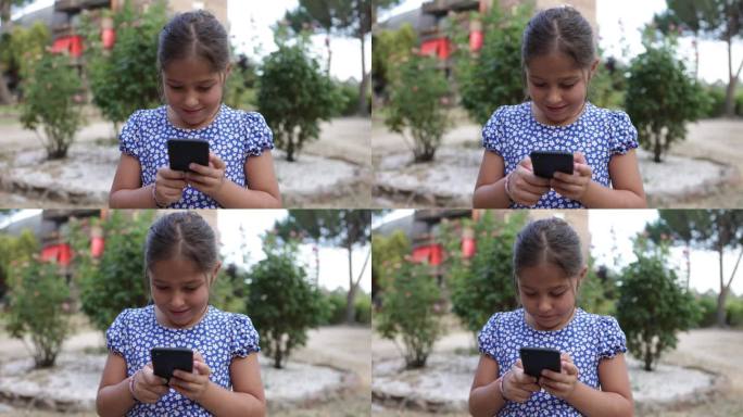 身穿蓝色印花连衣裙的黑发女孩在街上看手机。童年、电话、科技、网络、短信、快乐、放松、度假、生活理念。