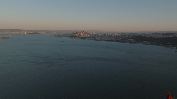 黄昏时大水面和大都市的航拍全景镜头。大型悬索桥顶部向后露出。美国加州旧金山