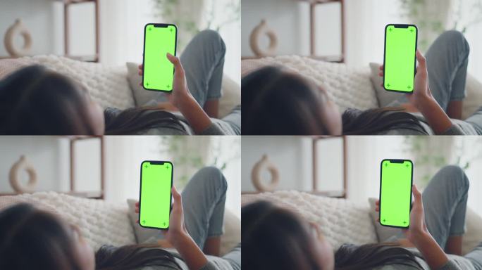 一个女人在家里客厅的沙发上休息时，使用带有色度键绿屏的智能手机，浏览社交媒体或网上购物的特写镜头-技