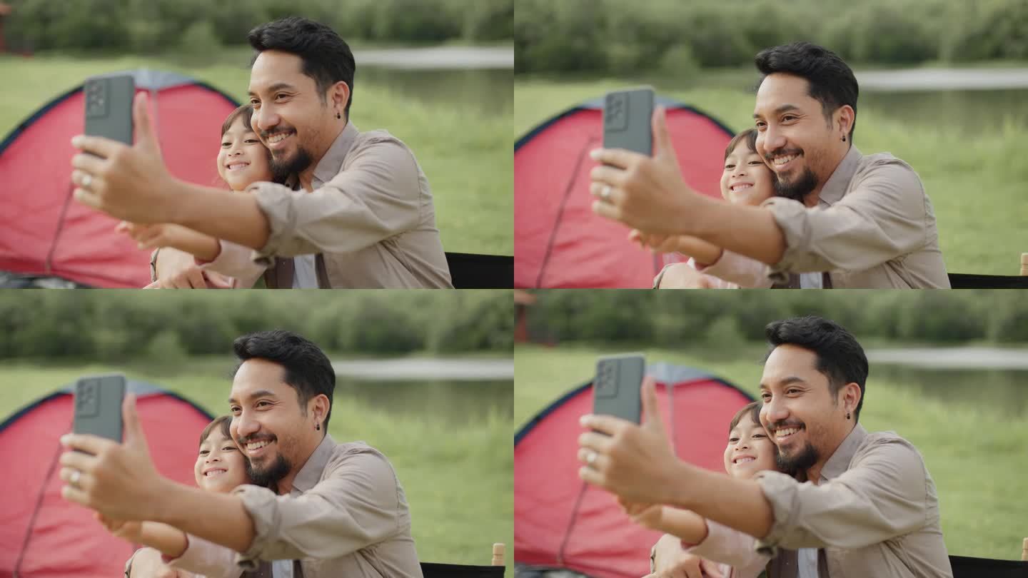 快乐的父亲用智能手机和女儿在草地上野餐和露营，并把照片上传到社交媒体上。