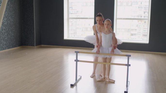 女芭蕾舞演员和女孩站在工作室的Barre