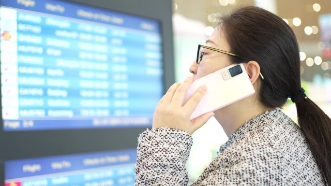 年轻的亚洲女商人用手机和顾客确认航班信息