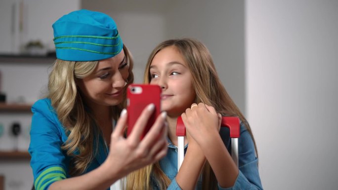 放大缩小，积极的空姐和女儿在智能手机上使用视频聊天应用程序交谈微笑的肖像。正面视图快乐的高加索美女和