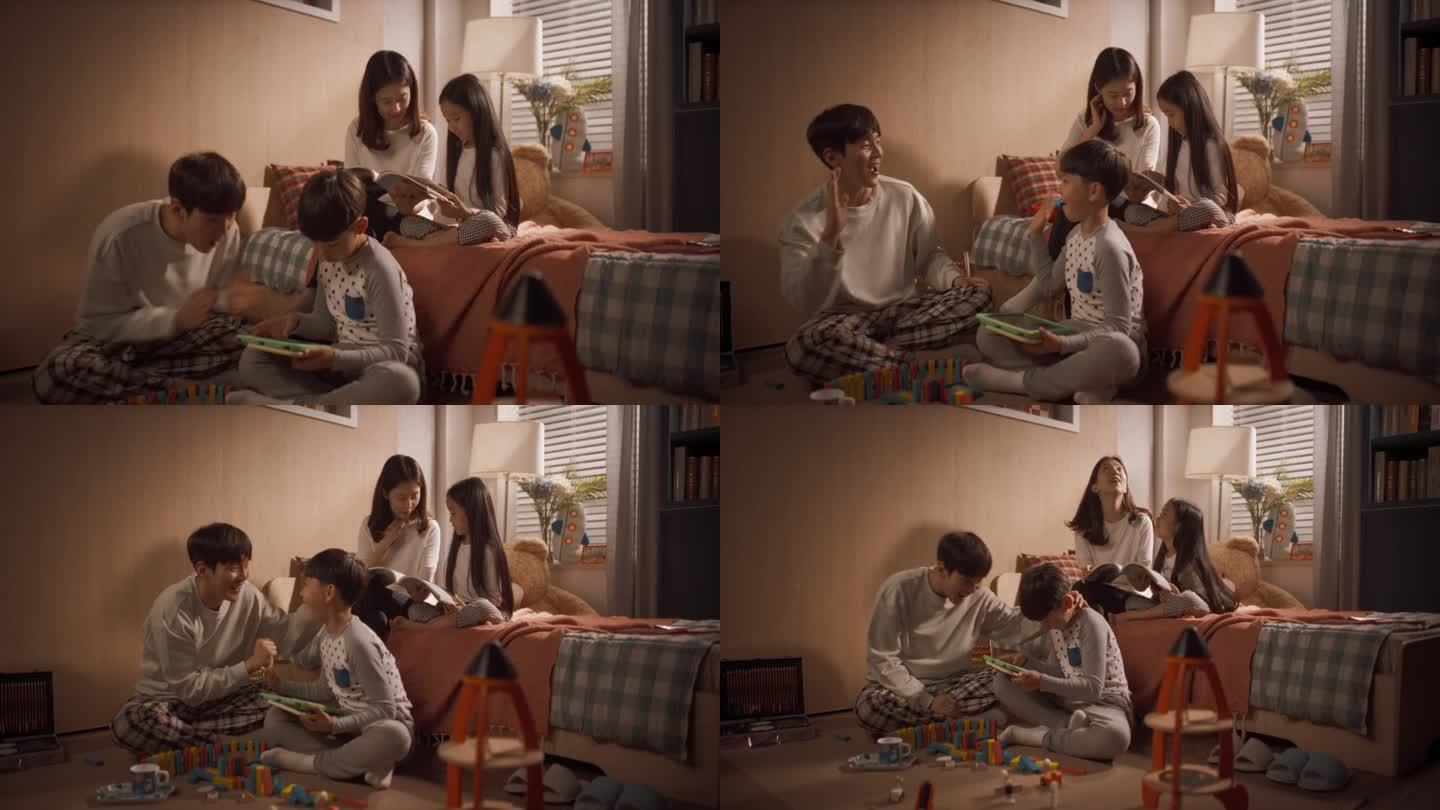 幸福的韩国夫妇与他们的孩子一起度过美好时光，一起玩有趣的游戏。父亲在为儿子欢呼，母亲在给女儿读一本迷