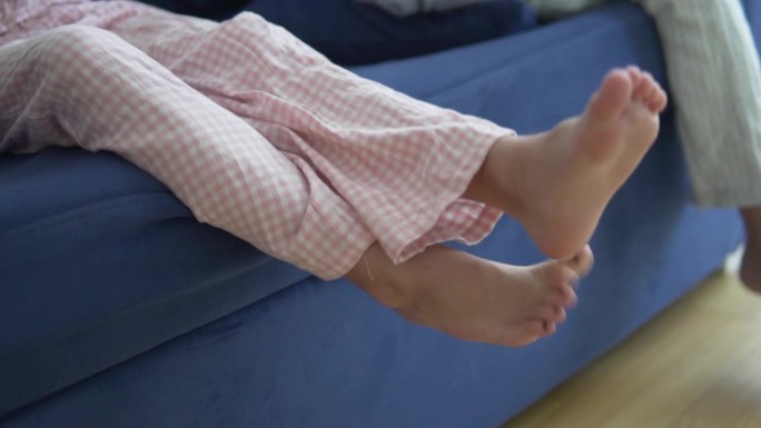 孩子们穿着粉色棉裤的腿挂在家里的沙发上