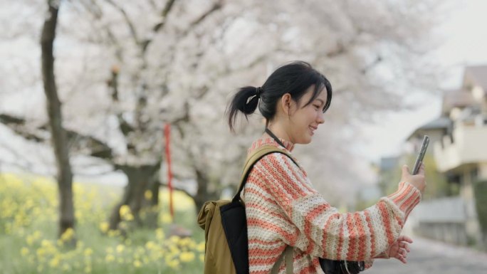 年轻女子在度假期间用智能手机与大自然中的樱花树自拍