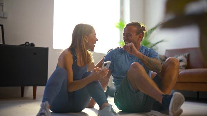 慢动作健身年轻夫妇一起使用智能手机在客厅地板上，休息一下家庭锻炼。健康的生活方式，人际关系，家庭生活