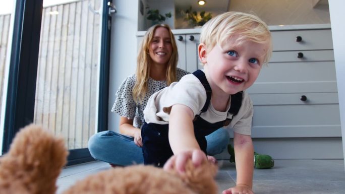 慈爱的母亲与年幼的儿子和玩具一起坐在家里厨房的地板上玩游戏