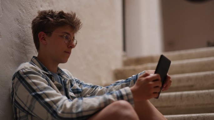 十几岁的男孩坐在楼梯上看电子书