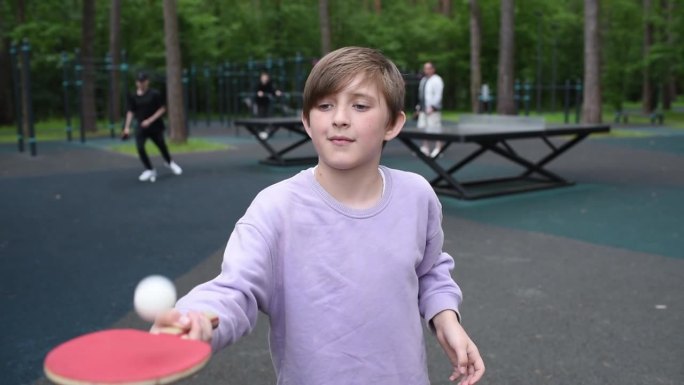 一个10岁的男孩在森林里的一个运动场上投掷并击中了一个乒乓球。孩子在训练打乒乓球