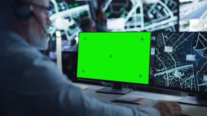 中年监控专家在绿屏模拟显示的电脑上工作。经理有效地多任务处理支持客户的电话和电脑工作