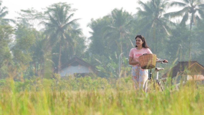 在村子里骑自行车，在农民收割水稻的背景下开心吗
