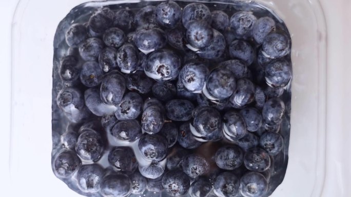 洗蓝莓。野生蓝莓的特写，慢慢地被水覆盖，慢慢地被冲走。厨房，水槽，水龙头。食用前的水果加工