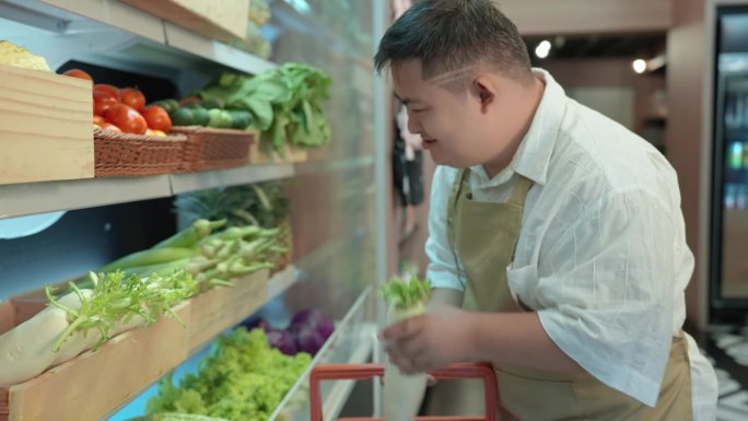 穿着围裙的亚洲残疾青年站在冰箱前采摘蔬菜和食品，然后送到顾客家。残疾超市。