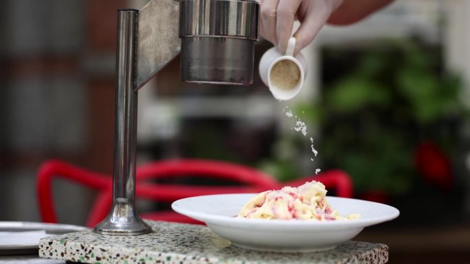 咖啡馆的工作人员将切碎的坚果洒在用水果糖浆浇上的成品冰淇淋上。