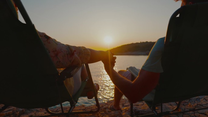 两人浪漫的日落。一对情侣手牵着手，在海岸线的椅子上放松