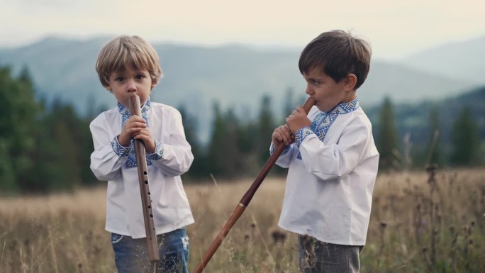 小男孩在喀尔巴阡山脉的草地上演奏木管木笛-乌克兰索皮卡。二重唱民乐概念。孩子们穿着传统的刺绣衬衫。