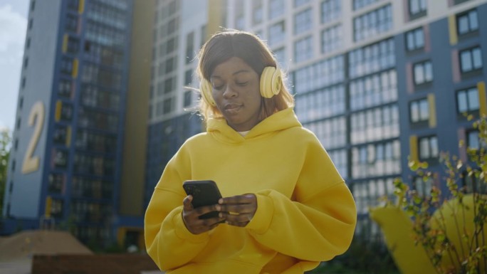 非裔美国少女在城市景观中使用电子设备，黑人妇女在听音乐