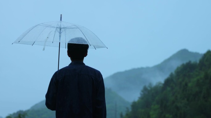 男人在雨天打着透明的伞看山