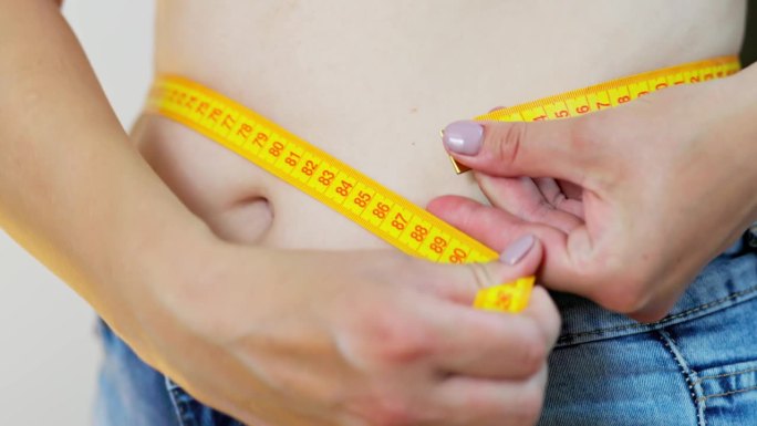 一个超重的女人用卷尺量腰围。超重，极端饮食概念