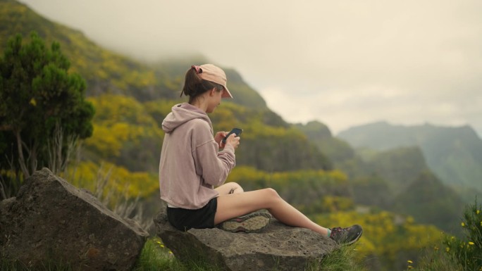 坐在世界之巅的女人。看着山下山谷的景色，发短信