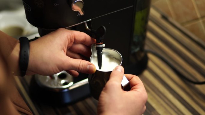 咖啡师用咖啡机在壶里使牛奶起泡