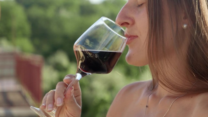 优雅的黑发女人在阳台或山间别墅的露台上喝着玻璃杯里的红酒。节日庆祝和暑假的魔力。