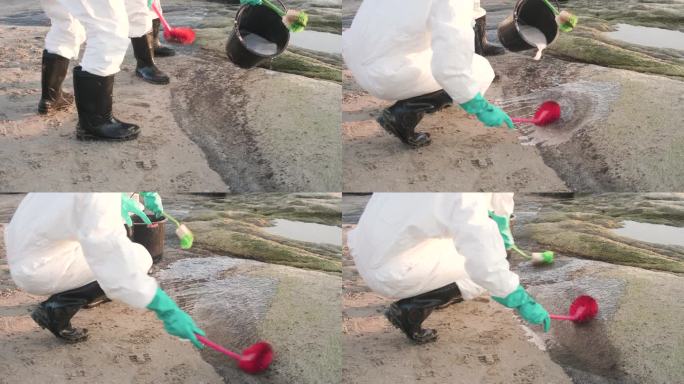 污染控制小组的个人防护用品用刷子清洁海滩上岩石上的石油泄漏