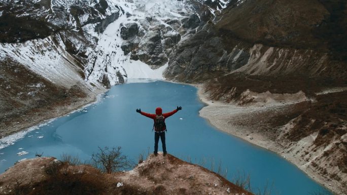 一个人站在山间湖泊前的悬崖边上