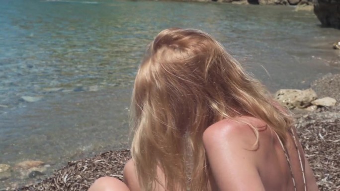 一位身材苗条、皮肤黝黑的女子躺在地中海多岩石的海岸上，现场摄像机跟踪拍摄。高角度视角的肖像，自信的游