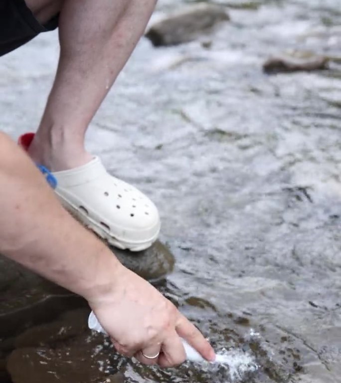 男孩站在山河附近的石头上，在水里洗电动牙盾。垂直视频