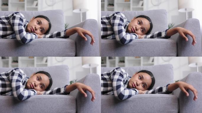 疲惫的非裔美国女孩躺在沙发上，感觉昏昏欲睡。感到沮丧，缺乏动力，悲伤，无聊。由于压力太大，她瘫倒在沙