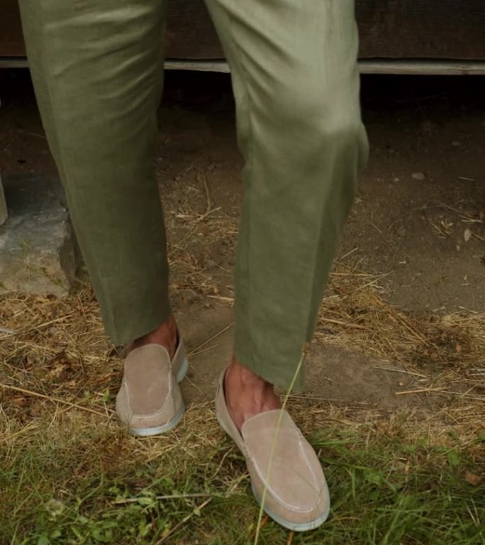 穿着绿色裤子和轻便鞋的男性腿。一个男孩模特站在木屋附近的地上。复古的风格。垂直视频