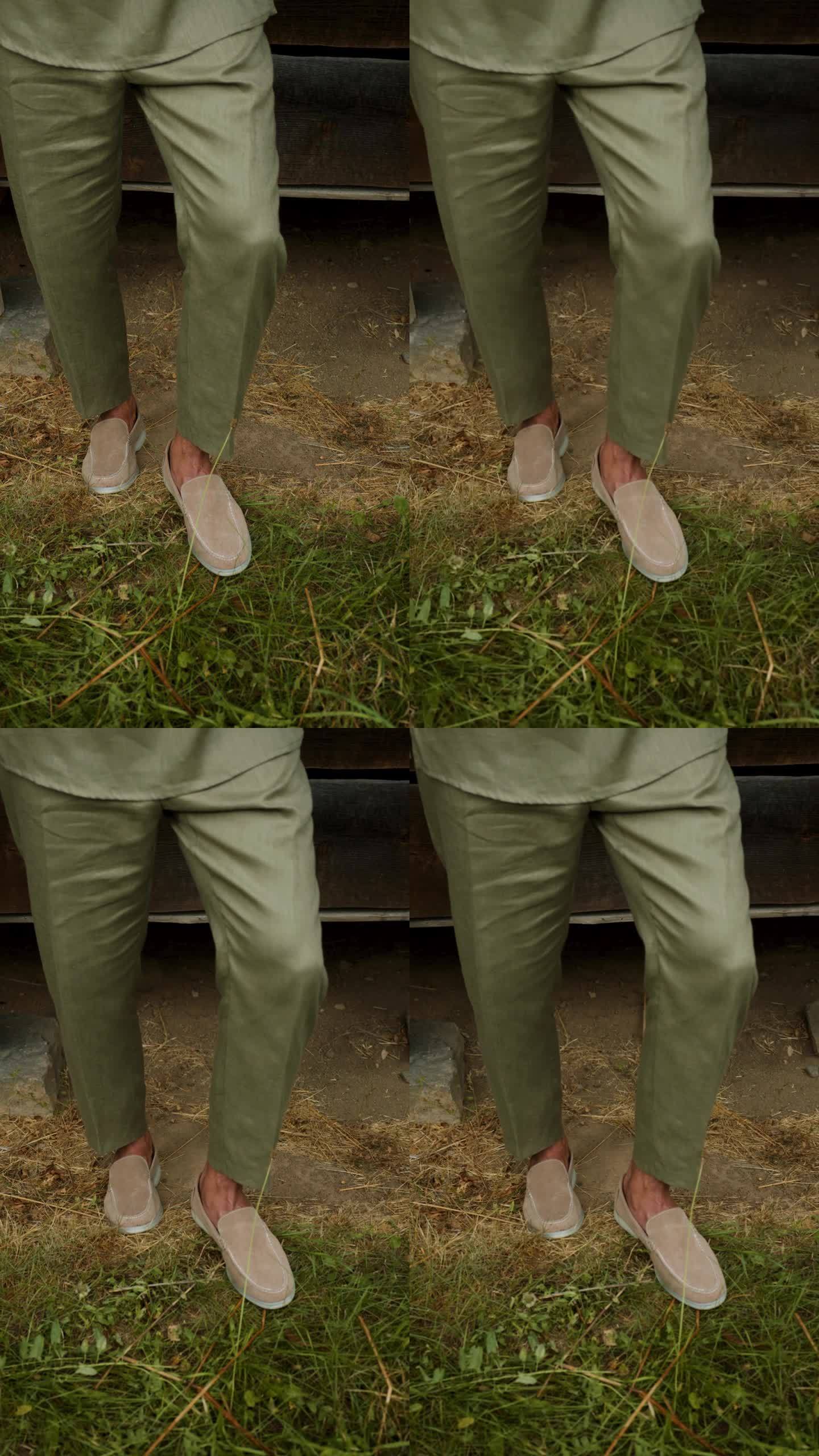 穿着绿色裤子和轻便鞋的男性腿。一个男孩模特站在木屋附近的地上。复古的风格。垂直视频