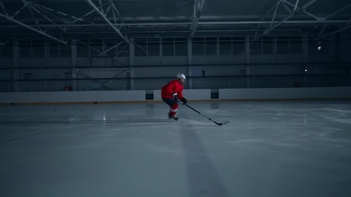 一段令人兴奋的视频，一名身穿红色运动衫的冰球运动员在黑暗的冰场上训练，快速移动并得分