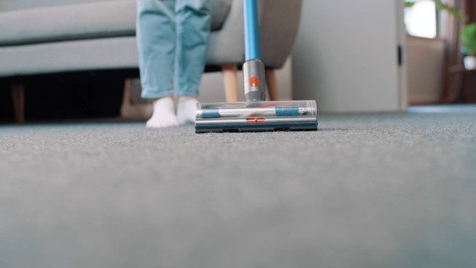 现代公寓中吸尘机吸尘地毯的近照。年轻女子在家客厅里保持房间整洁