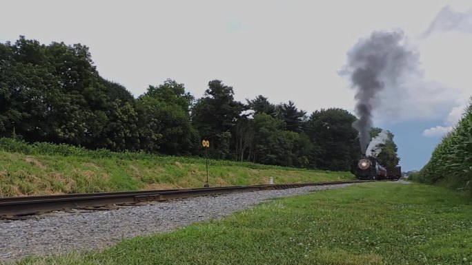 在一个阳光明媚的日子里，一列蒸汽客运列车在烟雾和蒸汽中启动的低角度