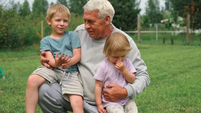 爷爷和孙子在公园散步时玩得很开心。快乐的家庭时光。老人爷爷抱着男孩和女孩。夏天的一天。微笑的老男人和