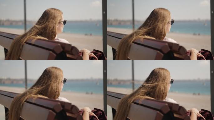 一位年轻女子坐在海边的长凳上，望着远方，风吹乱了她的长发。