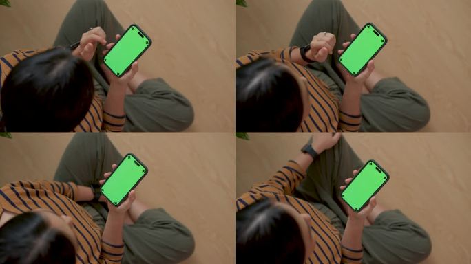 拿着绿屏智能手机的女人坐在家里的地板上。