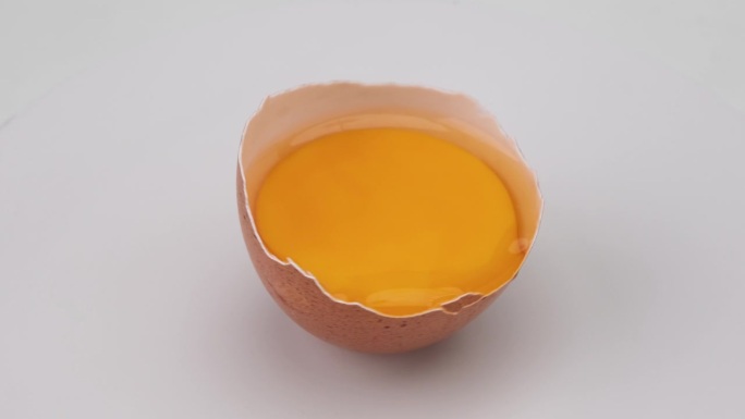在白色的背景下，鸡蛋的蛋壳正在翻转。蛋黄在蛋壳中的近景