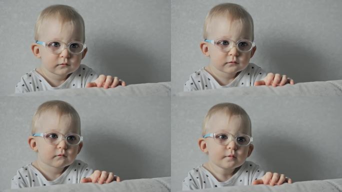 一岁大的斜视宝宝戴着眼镜在家里看电视。白种人婴儿有斜视，视力差或视力不好。白人小孩有眼疾。小孩子的肖