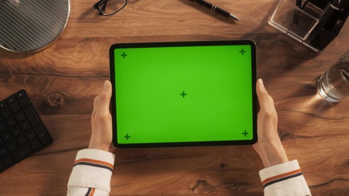 有创意的年轻艺术家手持平板电脑的静态镜头与绿色屏幕模拟显示在木制办公桌上。视频模板的数字演示，设计内