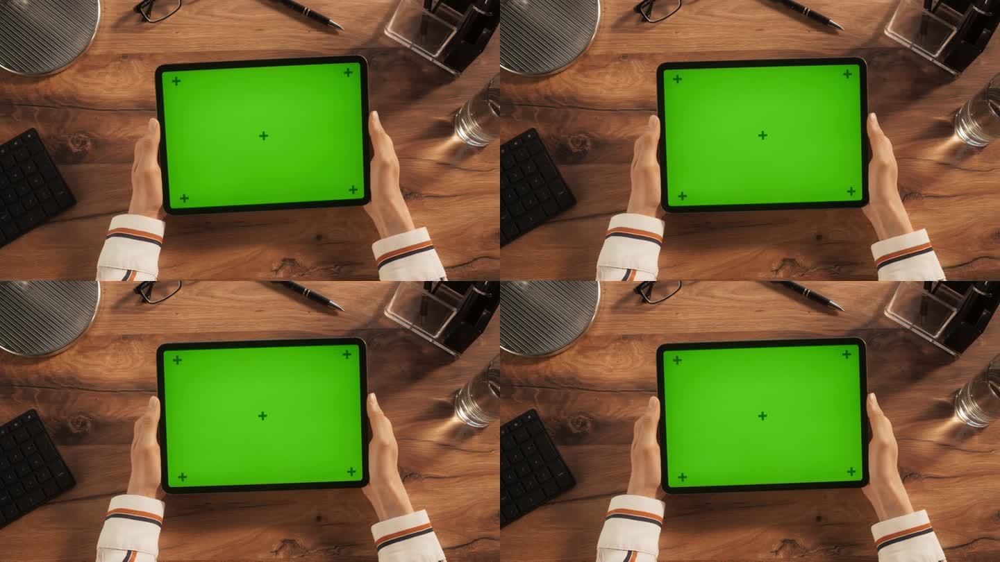 有创意的年轻艺术家手持平板电脑的静态镜头与绿色屏幕模拟显示在木制办公桌上。视频模板的数字演示，设计内