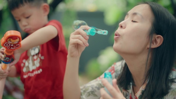 快乐时刻:亚洲男孩和妈妈在公园吹泡泡创造回忆-快乐的户外家庭时光