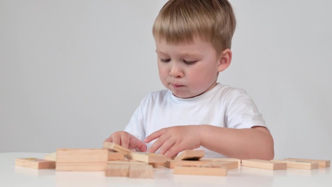 小男孩正在玩木块玩具，坐在白底的桌子旁，特写