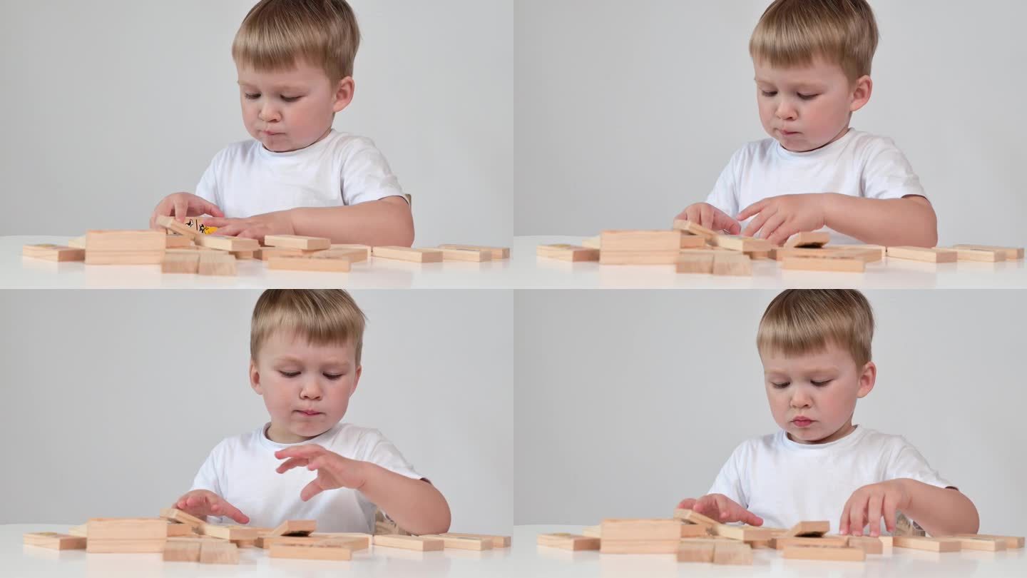 小男孩正在玩木块玩具，坐在白底的桌子旁，特写